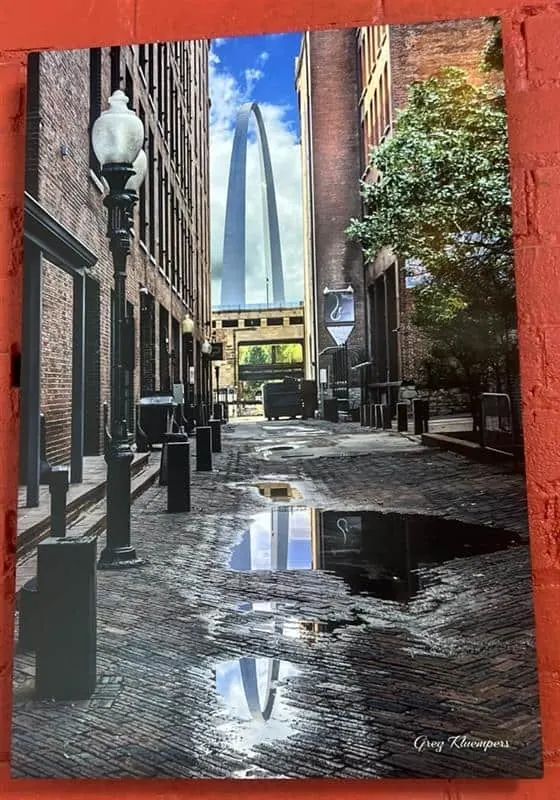 Rain-wet cobblestone alley in downtown St. Louis with the Gateway Arch at the end of the street.