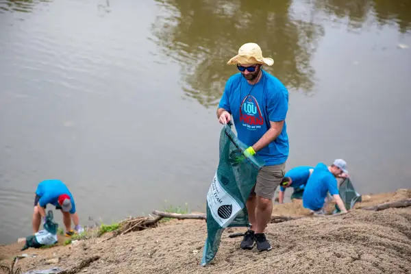 A volunteer in a straw hat bagging trash along the riverbank, 2022