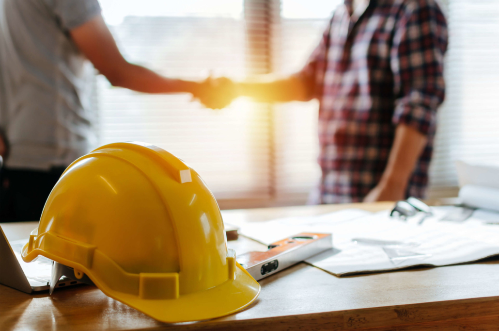 handshake deal at a construction site with a construction worker's hard hat