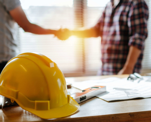 handshake deal at a construction site with a construction worker's hard hat