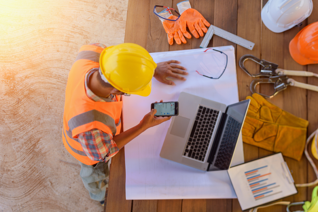 Top view of architectural engineer useing laptop on his blueprints with documents on construction site.