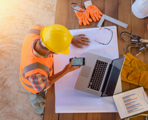 Top view of architectural engineer useing laptop on his blueprints with documents on construction site.