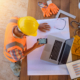 Top view of architectural engineer useing laptop on his blueprints with documents on construction site.