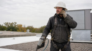 Commercial roofing contractor on a flat roof calling the facility manager who owns the roof budget
