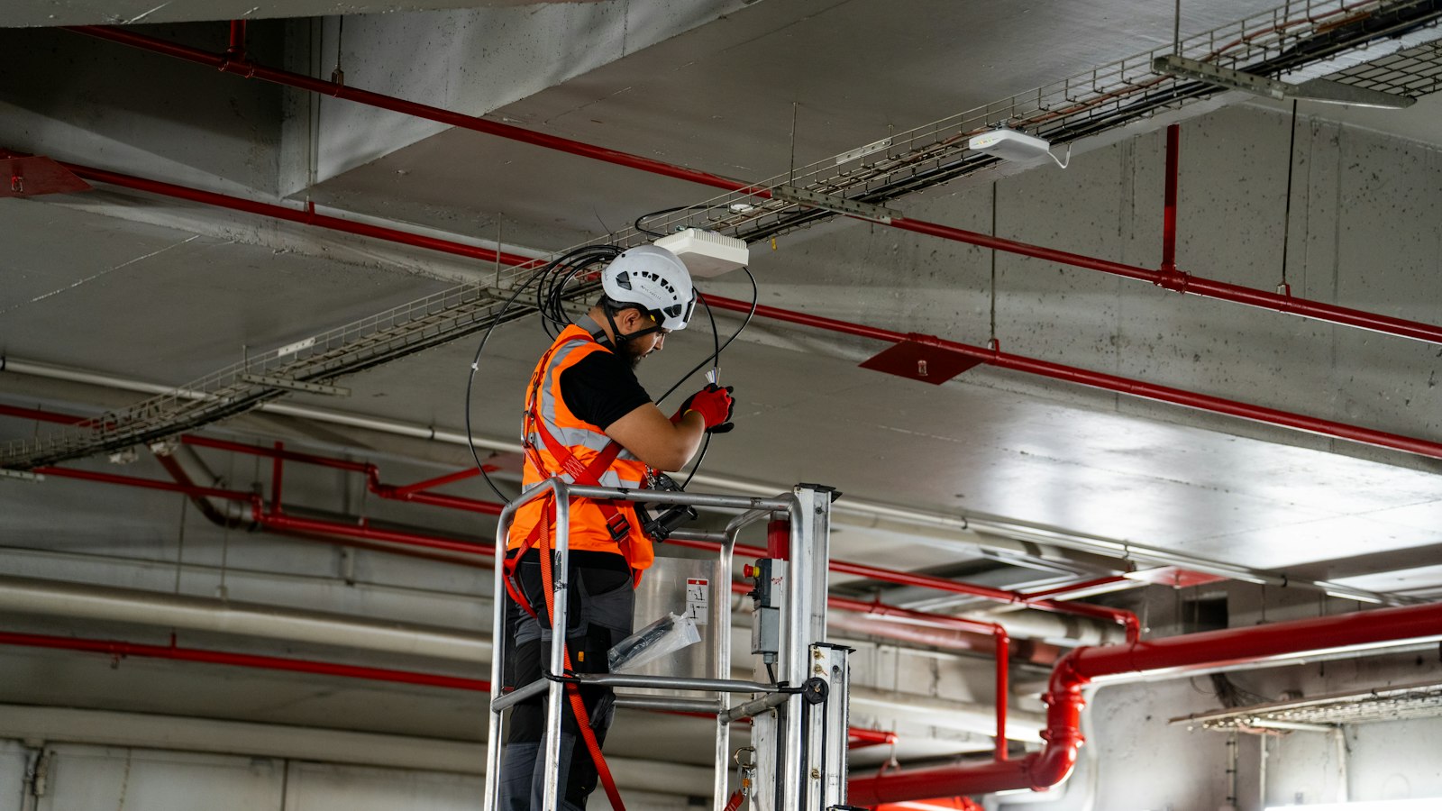 Technician on a lift working on overhead pipes in a commercial building