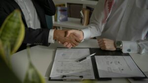 Two people shaking hands over a signed contract on a desk
